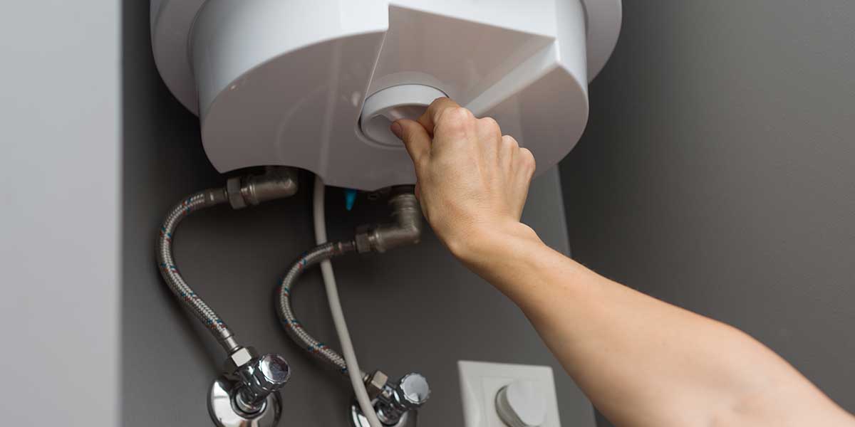Hand turning the temperature knob on a white water heater unit to fix sulfur and rotten egg water smells.